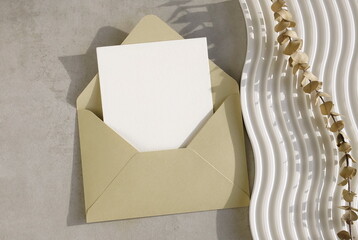 Beige envelope with blank paper card mockup  inside top view on beige textured background with sunlight shadow. Copy space.Wedding invitation mockup, greeting card, holiday concept.