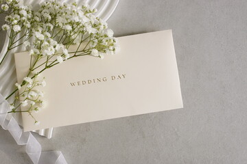 Wedding greeting card with a white flowers , ribbon, decor on light beige textured background. Wedding invitation with envelope.Copy space.