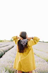 woman in yellow dress stands in lavender field, gently holding bouquet of lavender flowers. She appears serene and contemplative, enjoying beauty and fragrance of blossoms around her.