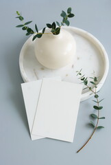 Greetings card blank mockup and eucalyptus leaves in a vase on light blue background with copy space.Top view. Empty blank, card mock up, template, birthday, holiday. 
