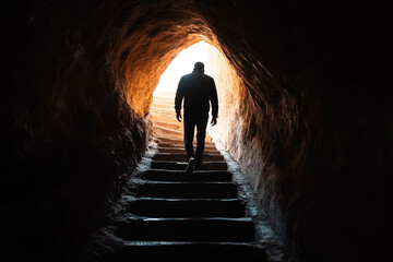 Man walking up stone steps towards light in dark cave
