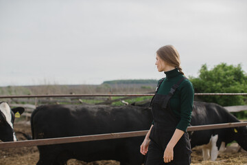 Young female farm worker near a paddock with cows outdoors.