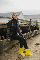 A young beautiful woman farmer poses against the background of a paddock with calves on a livestock...
