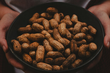 Hands holding peanuts in shell in a bowl. Close-up. Horizontal background. Unshelled peanut, groundnut, goober