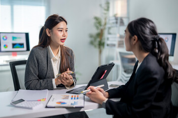 Two women are sitting at a desk, talking to each other