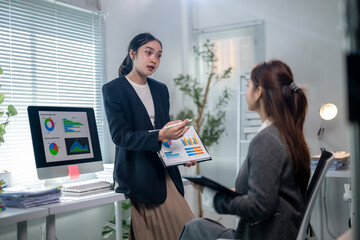 Two women in a business setting, one holding a presentation