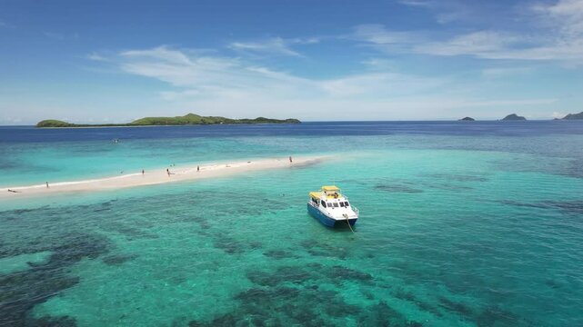 Boat anchored off tropical island sandbar and clear blue water on sunny day - aerial