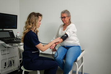 Young nurse using sphygmomanometer, taking blood pressure of a senior woman patient during medical...