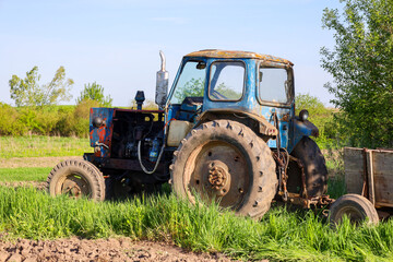 Naklejka premium Old, abandoned tractor rusts in green grass under a clear sky. Agricultural machinery neglected by time, showing wear and age.