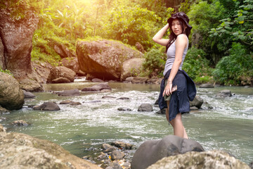 Young Asian Woman Standing on Rocky Riverbank in Forest During Outdoor Adventure