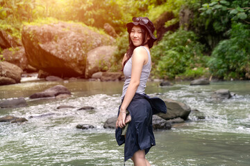 Smiling Asian Woman in Sunhat Looking Back in Lush Green Forest with Sunlight