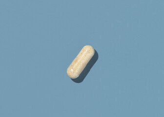 Beige Medical capsule on blue top view, hard shadows. Taking dietary supplements