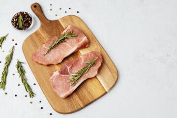 Freshly prepared pork chops with rosemary on a wooden cutting board