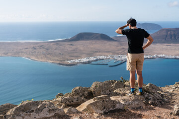 Tourist man hiker standing on the top of the mountain looking down on the sea and island