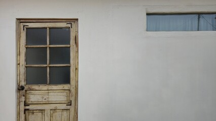 1️⃣ A rustic wooden door with a textured glass pane sits beside a small window on a white wall, offering a charming and nostalgic aesthetic.