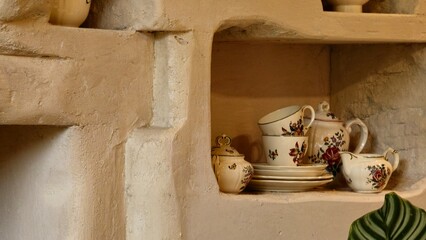 Rustic shelves with vintage floral ceramics, including teacups and pitchers. The textured wall and soft lighting enhance the cozy, nostalgic feel, ideal for decor and editorial use.