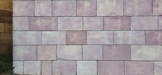 A staggered-pattern stone wall composed of rectangular blocks with a purple hue, arranged in an...