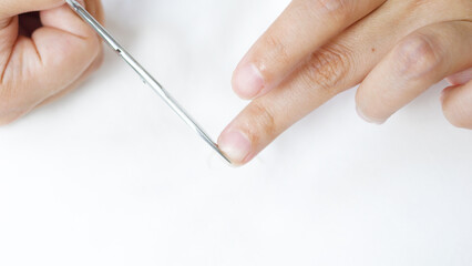 Woman cutting fingernails with small scissors on a clean white background, engaging in a personal hygiene routine that emphasizes nail care and beauty maintenance