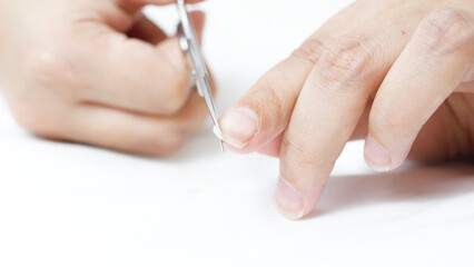Woman cutting fingernails with nail scissors on a clean white background, engaging in a fundamental hygiene routine that emphasizes self care and personal grooming