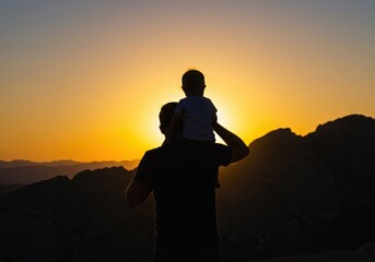 Silhouette of father and child on shoulders against a vibrant sunset sky view