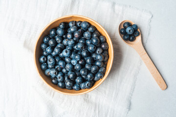 Fresh blueberries in wooden bowl on light fabric background