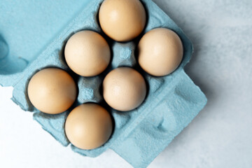 Brown chicken eggs in a blue carton box on light blue background, top view