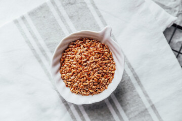 Brown flaxseeds in a white bowl on a linen towel in a kitchen setting