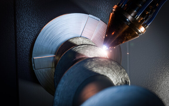 High-precision CNC 3D printing process of a large metal auger using a rotary axis. The footage shows additive manufacturing with a robotic laser head building up metal layers on a rotating part.