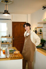 Young man wearing apron smiling in modern kitchen, ready to cook a meal at home.