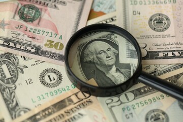 Big amount of United States USD dollar bills and magnifying glass
