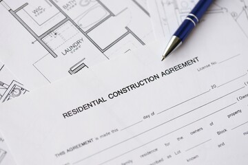Pen on residential construction agreement and planning blueprints of residential building project