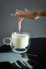 Organic milk, with drop dripping from fingertip into clear glass mug, natural goodness and...