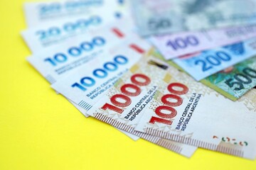 Argentine pesos money bills in big amount lies on yellow color table close up