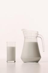 Milk in transparent glass stands beside matching pitcher in simple studio setup. Concept of drink, organic food, aesthetics, advertisement