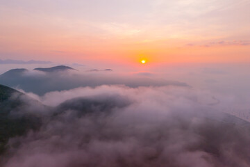 Morning light from the sun dawn on the coast with mountains and hills shrouded in wet clouds and fog, warm tones summer aerial above point view landscape