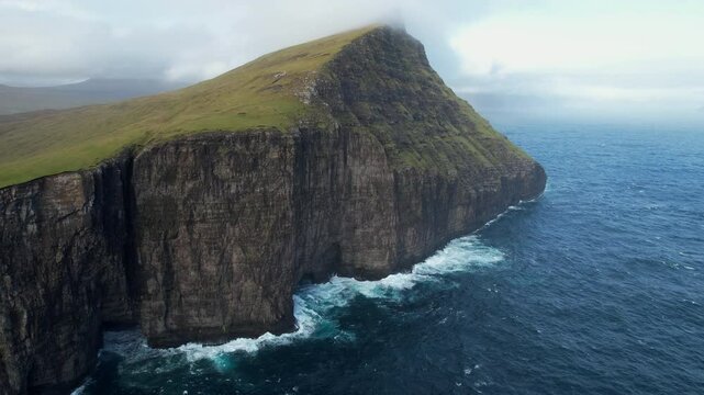 Green cliffs of faroe islands meet powerful ocean waves in a breathtaking display of nature's raw beauty