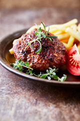 Fried hamburger steak with tomatoes and french fries. Rustic background. Close up.