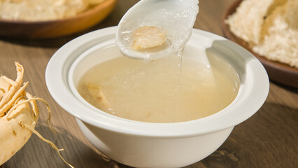 Close-up of a spoon scooping bird's nest strands out of a porcelain bowl. The bowl of the bird's nest is opaque white in color and has a thick texture. Bird's nest is a nutritious source of protein.