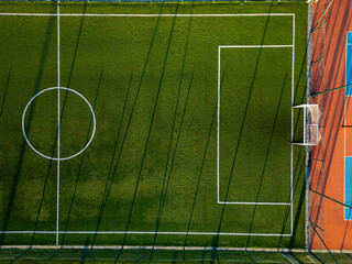 Aerial view of a youth soccer training session on a green field with long shadows cast by players in the late afternoon sun