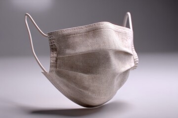 Close-up of a stylish fabric face mask for protection against viruses and pollution, reusable and fashionable alternative with a neutral color on grey background.