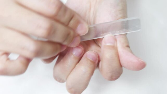 Professional manicurist using glass nail file, gently polishing and shaping fingernails to achieve smooth, refined nail contours with precise technique
