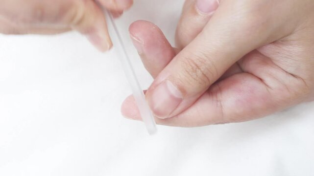 Close up of woman filing fingernails with glass tool, performing precise nail shaping and smoothing for professional manicure care