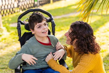 Happy child with disability interacting with mother outdoors in wheelchair