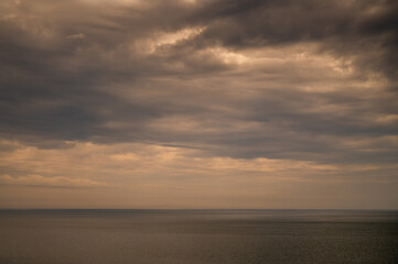 Sun between dark storm clouds over ocean. Dramatic seascape. Clouds and rain flurry over sea.