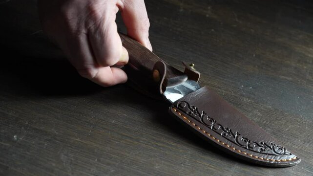 Man's hand takes a forged sharp knife from the wooden table, close up. Iron knife with shiny blade  in male hands