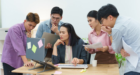 Group of colleagues collaborating in a modern office setting while discussing project details and analyzing data on a laptop