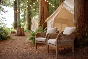 Fototapeta premium Luxurious forest glamping deck featuring two elegant chairs beside a cozy tent surrounded by lush trees and soft lighting creating a tranquil atmosphere