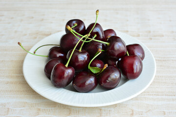 A heap of dark juicy cherries on a white plate
