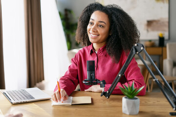 Happy young woman recording podcast and taking notes