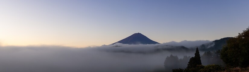 Serene early morning panorama of Mount Fuji surrounded by mist as the first sunlight illuminates...
